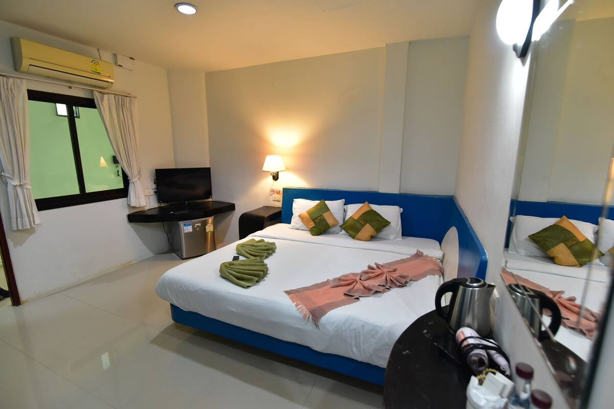 A hotel room with a bed, a TV, a lamp, and a mirror.