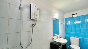 Un baño con paredes de azulejos blancos, zona de ducha con azulejos azules, lavamanos blanco y un inodoro.