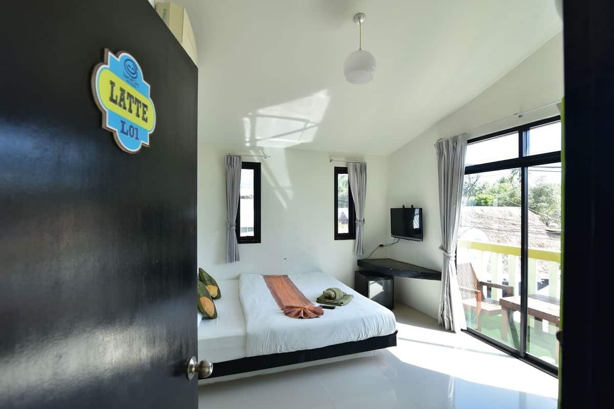 A bedroom with a bed, a desk, a TV, and a window with a view.