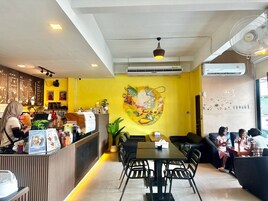 Interior de una cafetería con mostrador, zona de mesas y un mural en la pared.