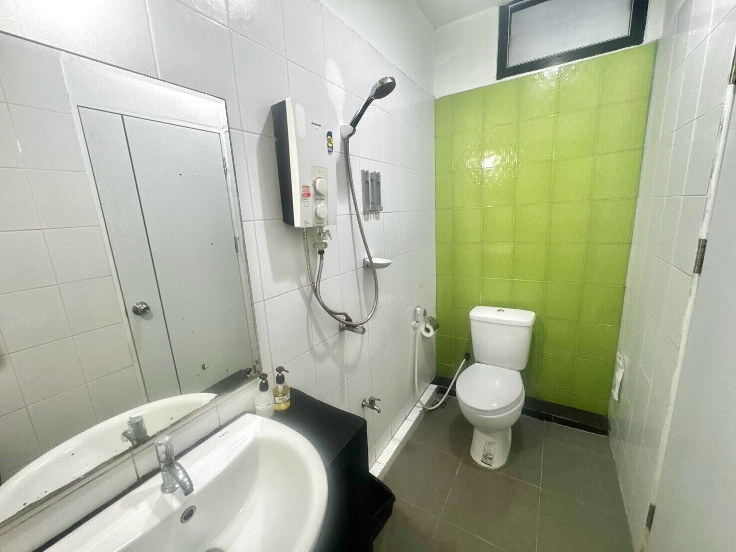 Un baño con lavamanos blanco, un espejo, ducha con cabezal de ducha manual y un inodoro.