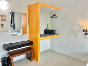 A hotel room with a black console table, a wooden bench, a mirror, a hanging coat rack, a small shelf with a radio, and a wall-mounted lamp. - Harmony Bed and Bakery (Koh Lipe)