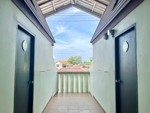 A corridor with two doors, each marked with a 'LATTE' sign, leading to a balcony with a view of buildings and a red-roofed structure. - Harmony Bed and Bakery (Koh Lipe)