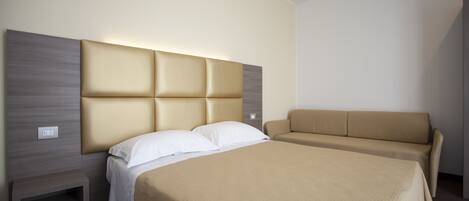 A hotel room with a large bed, a sofa, and a nightstand.