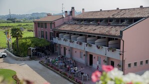 A building with a terracotta-tiled roof, outdoor seating area with tables and chairs, and a garden with flowers. - Hotel Bella Lazise (Lazise)