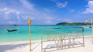 Una playa con un letrero que dice "BUNDHAYA VILLAS" y un bote en el agua.