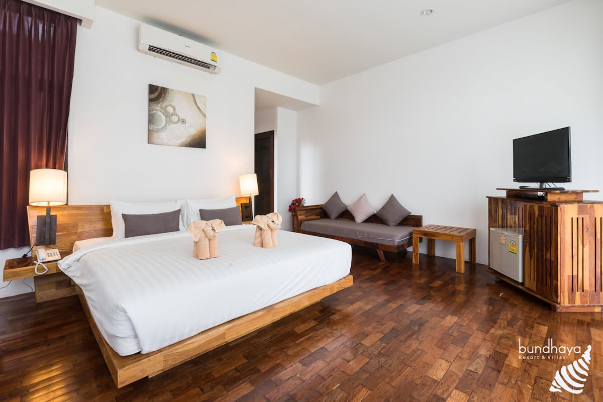Hotellihuone, jossa on suuri sänky, televisio, puinen kaappi ja sohva.