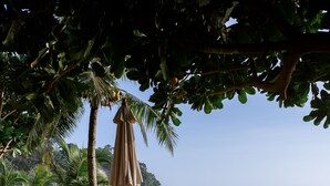Una terraza de madera con sillones de descanso y una sombrilla, con vista a una playa con palmeras y al océano.