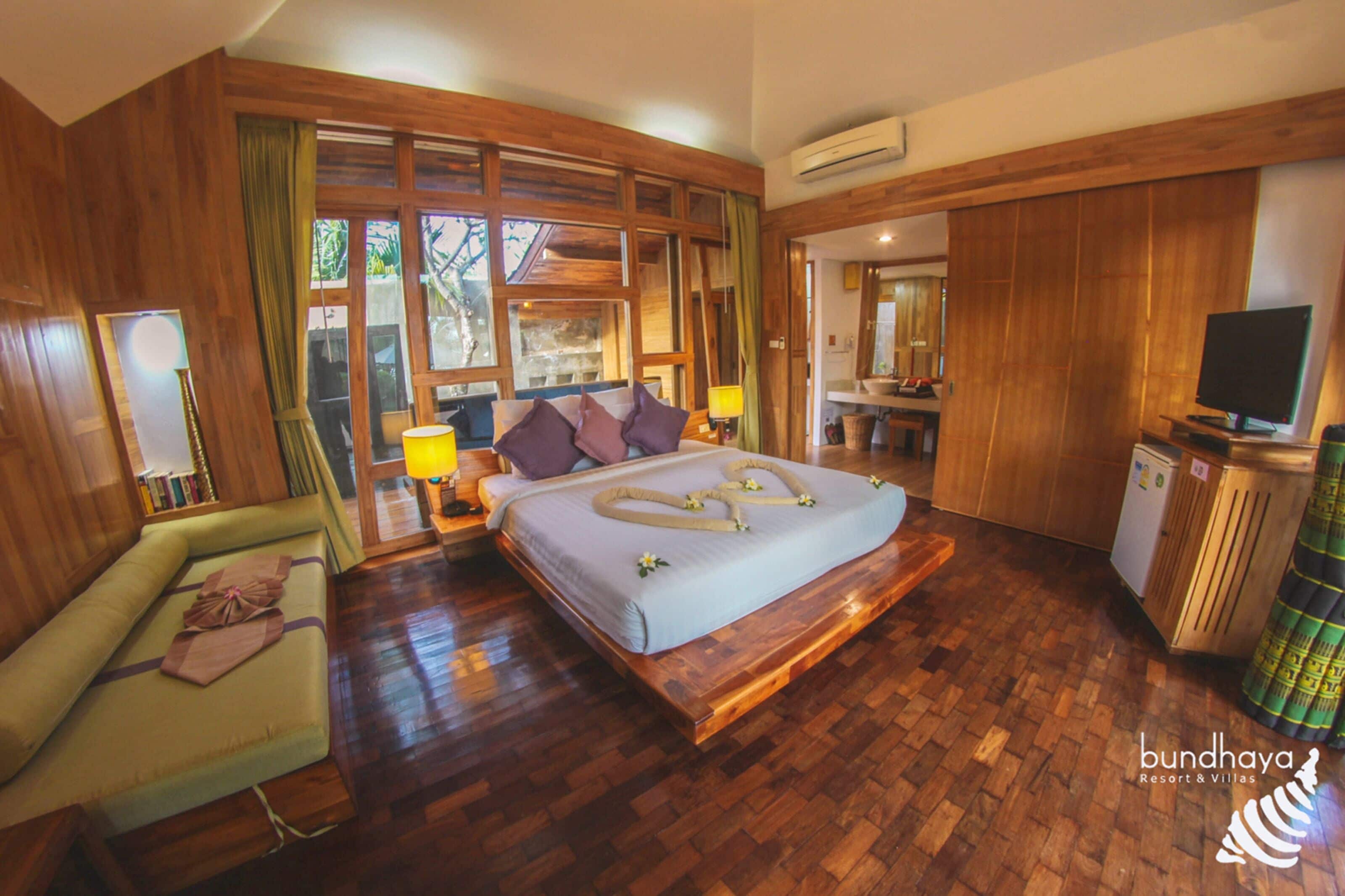 A spacious bedroom with a large bed, a green sofa, wooden flooring, and a television.