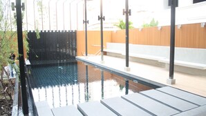 An outdoor swimming pool with a wooden deck, metal railings, and a bench.