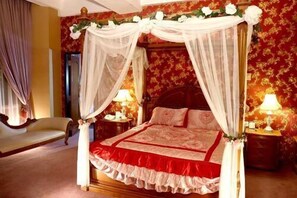 Uma cama com dossel e cortina, duas mesas de cabeceira com abajures e detalhes florais.