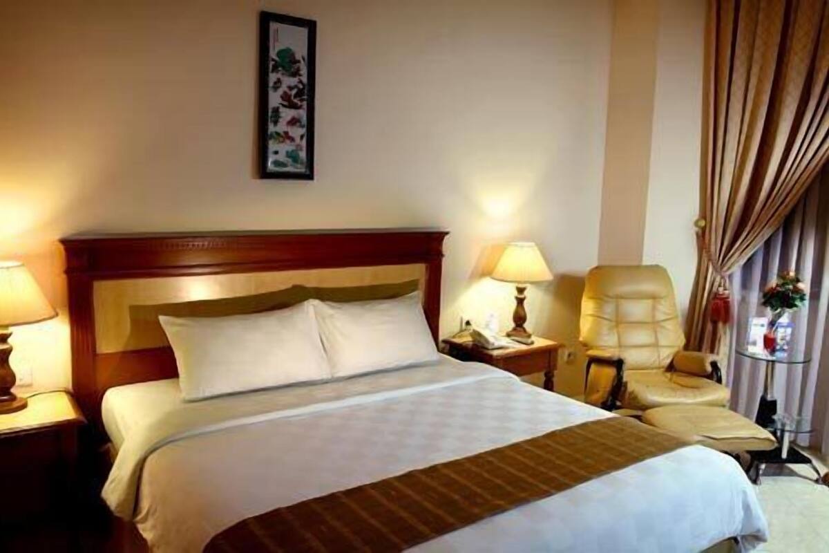 A hotel room with a large bed, two bedside tables with lamps, a chair, and a curtain.