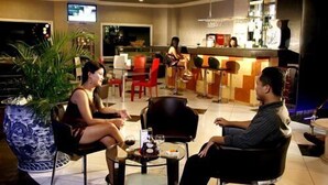 A modern bar area with a seating arrangement, a television screen, and a potted plant. - Hotel Grand Tiga Mustika (Balikpapan)