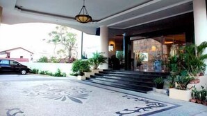 A hotel entrance with a patterned floor, steps leading up to the door, and potted plants. - Hotel Grand Tiga Mustika (Balikpapan)