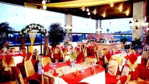 A banquet hall with round tables covered in red tablecloths, gold sashes, and white centerpieces. - Hotel Grand Tiga Mustika (Balikpapan)