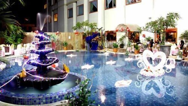 A swimming pool with a fountain, surrounded by potted plants and a building with multiple windows. - Hotel Grand Tiga Mustika (Balikpapan)