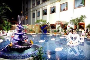 A swimming pool with a fountain, surrounded by potted plants and a building with multiple windows. - Hotel Grand Tiga Mustika (Balikpapan)