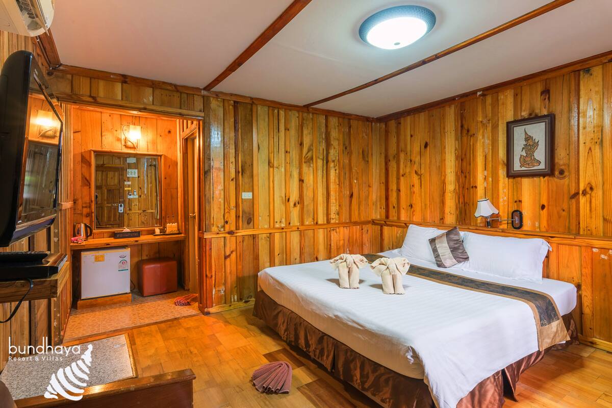 Een kamer met houten lambrisering, een bed, een televisie en een klein keukentje.