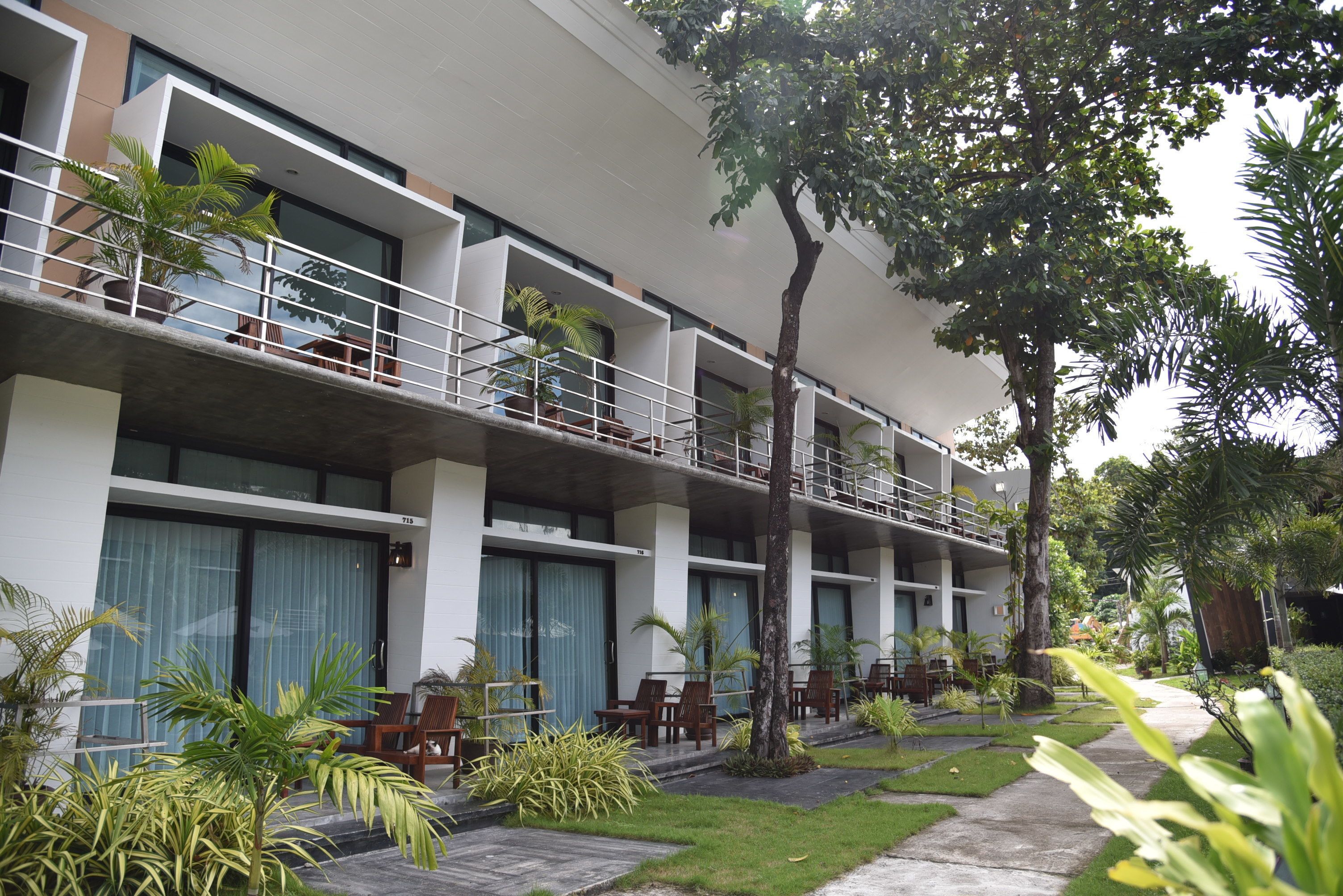 A modern hotel with multiple balconies, outdoor seating, and lush greenery.
