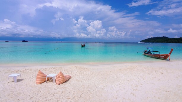 A beach with clear turquoise water, a boat, and a row of white and orange striped beach chairs. - Bundhaya Resort Koh Lipe (Koh Lipe)
