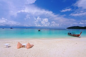 Une plage à l’eau turquoise et limpide, un bateau et une rangée de chaises de plage rayées de blanc et d’orange.