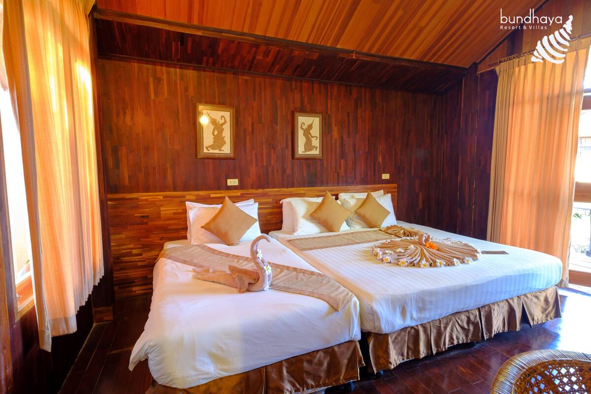 Een hotelkamer met twee bedden, houten wanden en gordijnen.