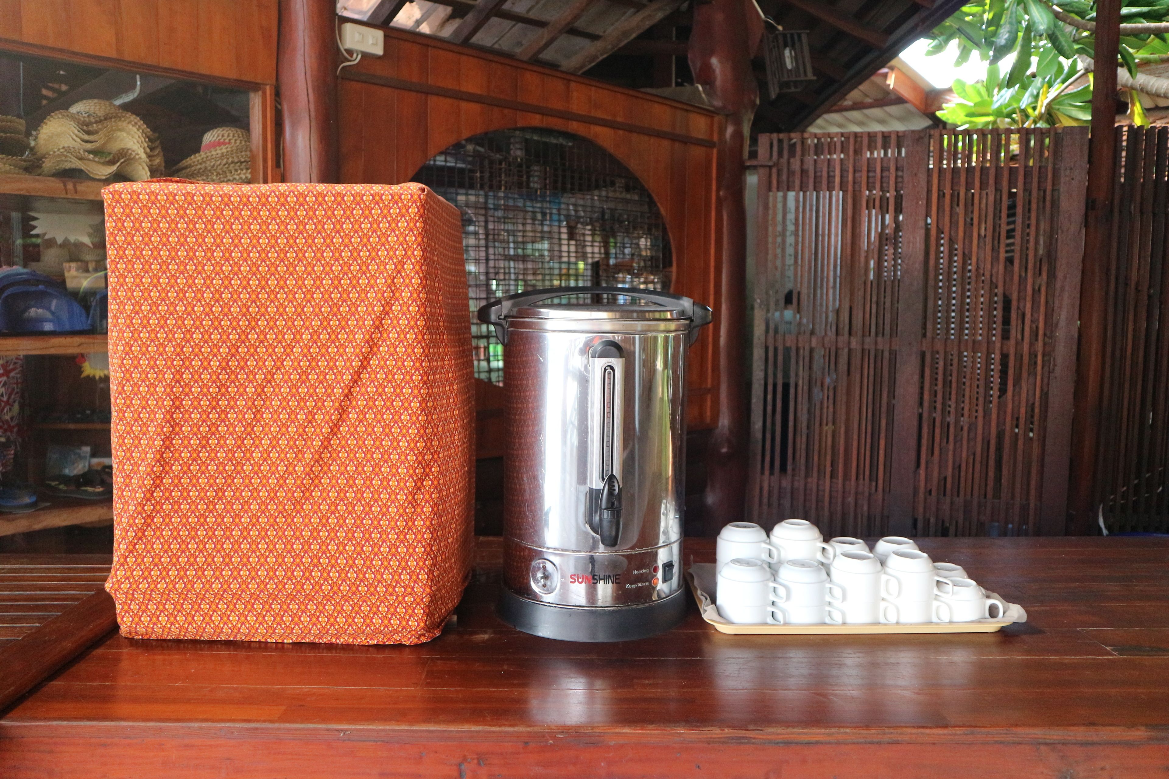 A kitchen area with a stainless steel coffee maker, a patterned orange container, and a tray of white cups.