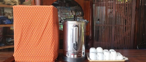 A kitchen area with a stainless steel coffee maker, a patterned orange container, and a tray of white cups.