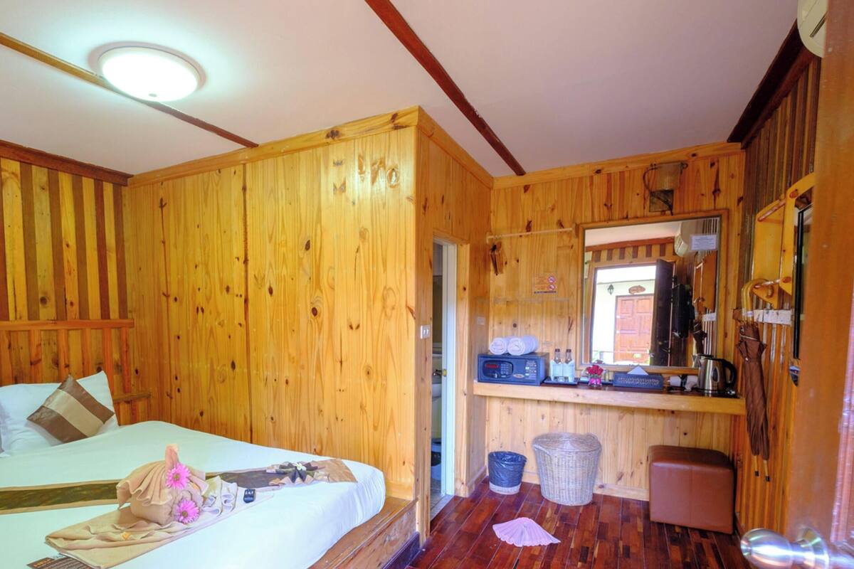 Een houten kamer met een bed, een klein keukentje en een spiegel.