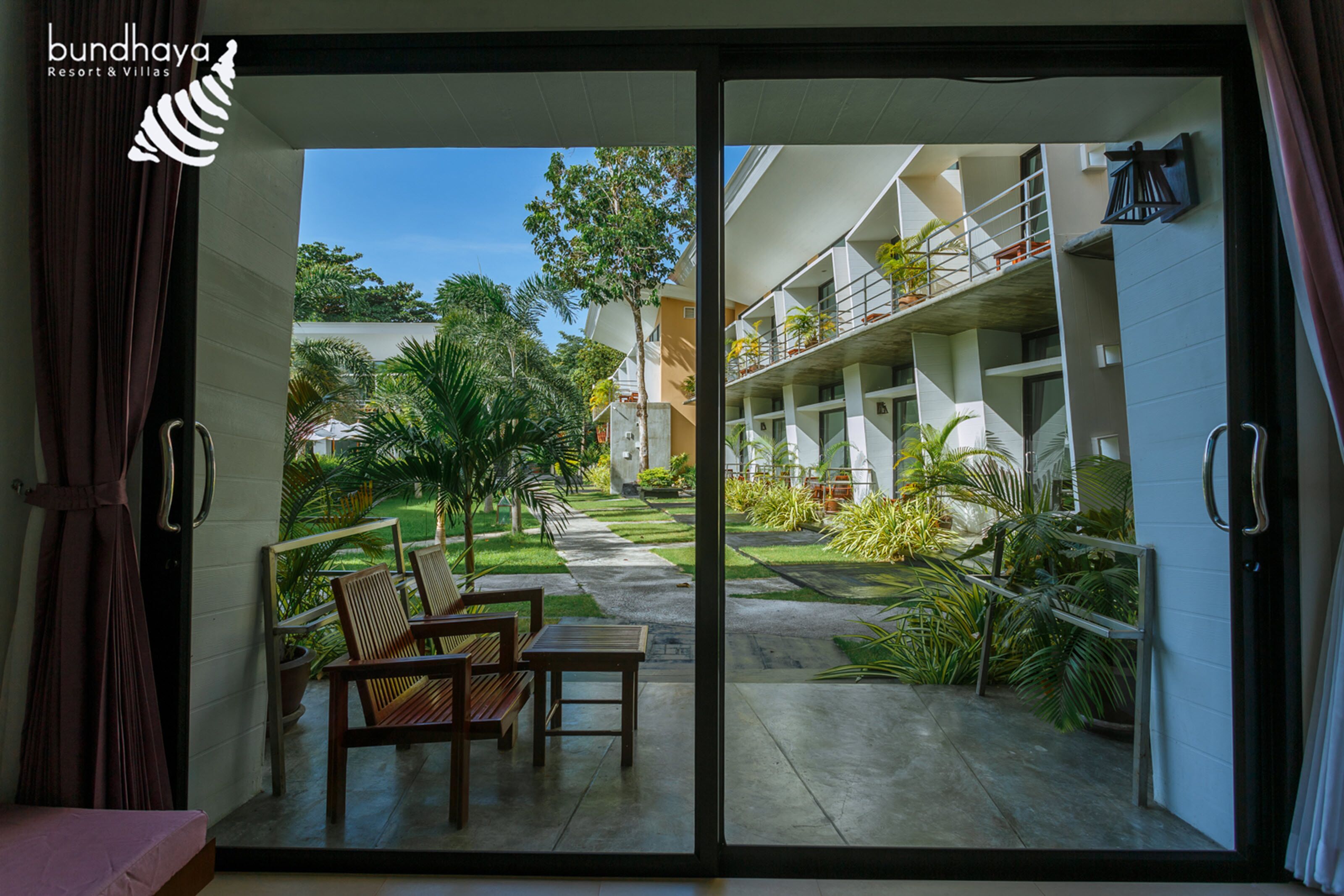 A room with a sliding glass door leading to a courtyard with outdoor seating and a view of a building with balconies.