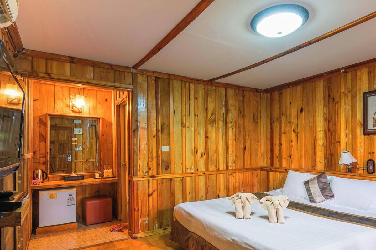 Een kamer met houten lambrisering, een bed, een bureau met een computer, een televisie en een kleine koelkast.
