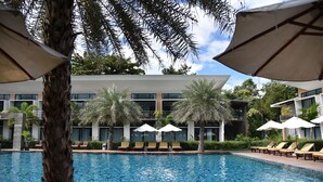 A swimming pool with lounge chairs and umbrellas, surrounded by palm trees and modern buildings. - Bundhaya Resort Koh Lipe (Koh Lipe)