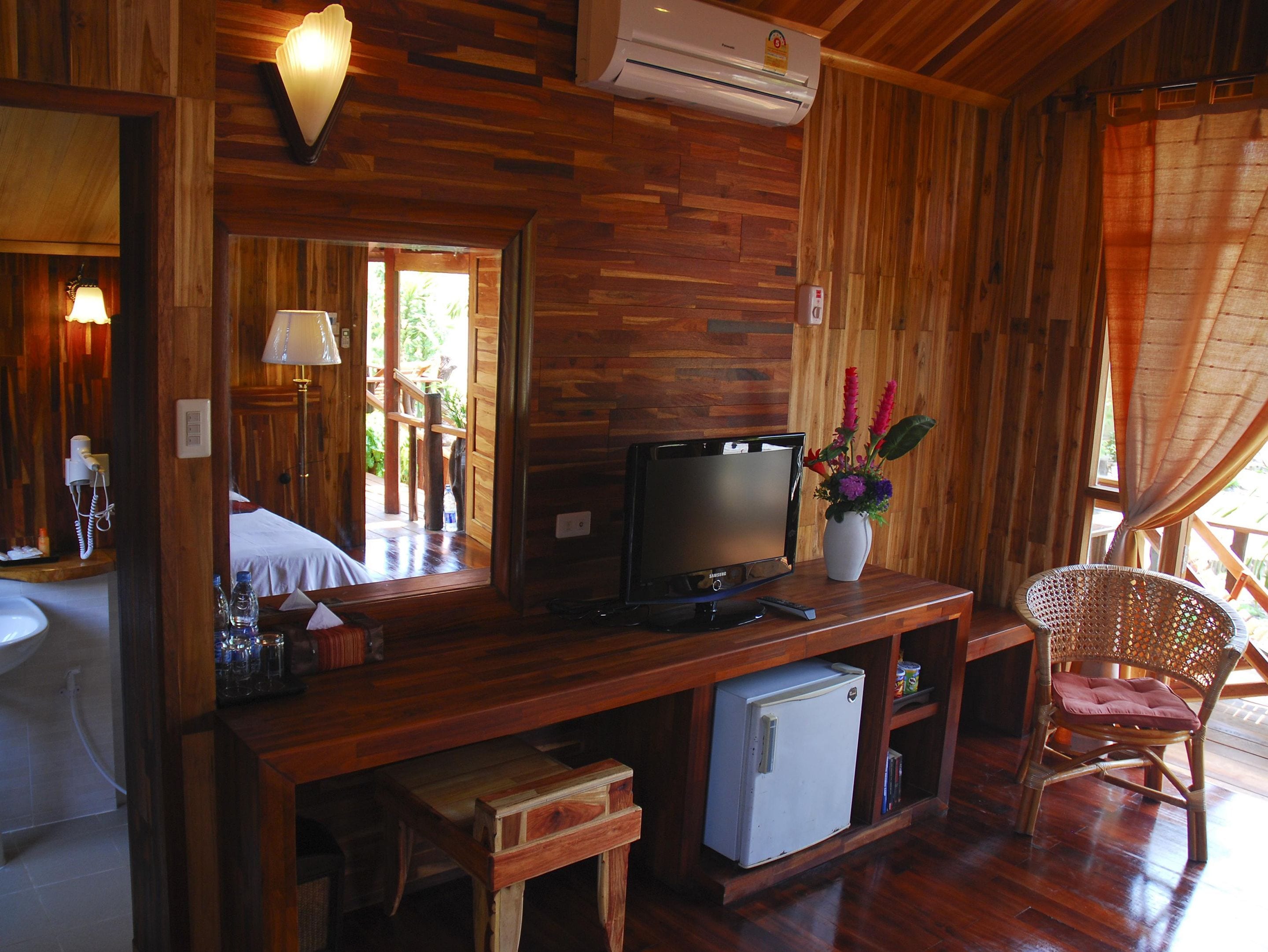 A wooden interior with a television, a small refrigerator, a chair, and a mirror.