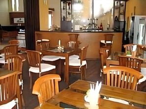 Een restaurant met houten tafels en stoelen, een bar en uitzicht op een gebouw door de ramen.