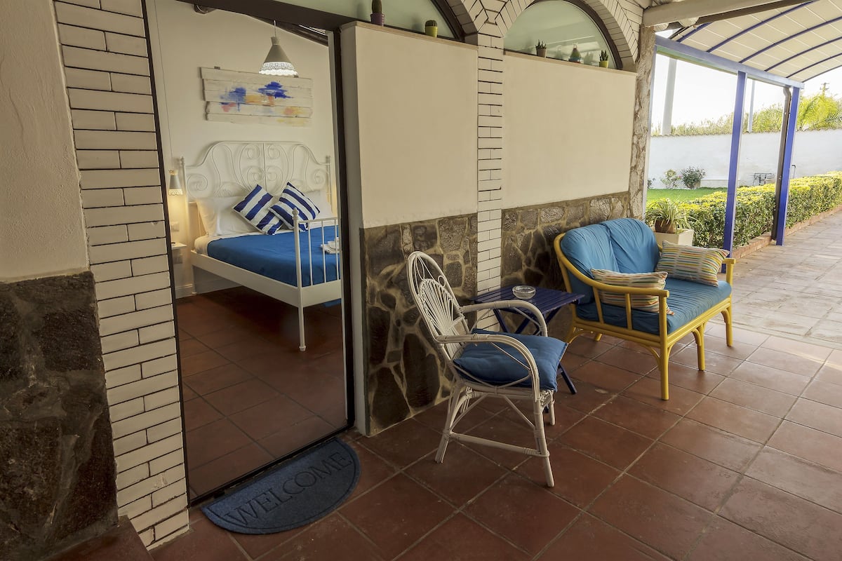 Une chambre avec un lit, deux chaises, une petite table et une vue sur un jardin.