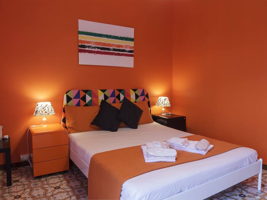 A hotel room with a bed, two bedside tables, a nightstand, a lamp, and a colorful headboard.