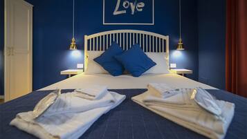 Een net opgemaakt bed met blauwe kussens, twee bedlampjes en een houten bordje met de tekst 'Love' aan de muur.