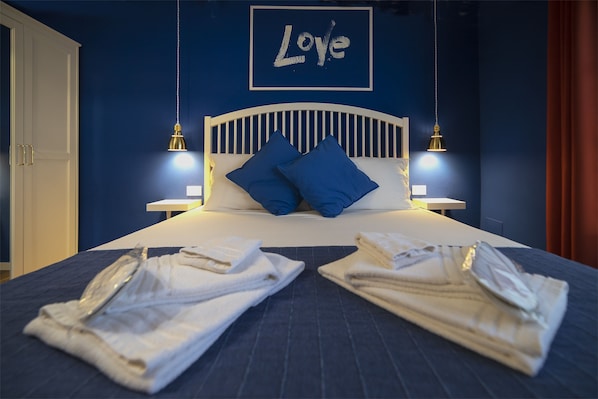 A neatly made bed with blue pillows, two bedside lamps, and a framed 'Love' sign on the wall. - B&B Le Saline (Syracuse)