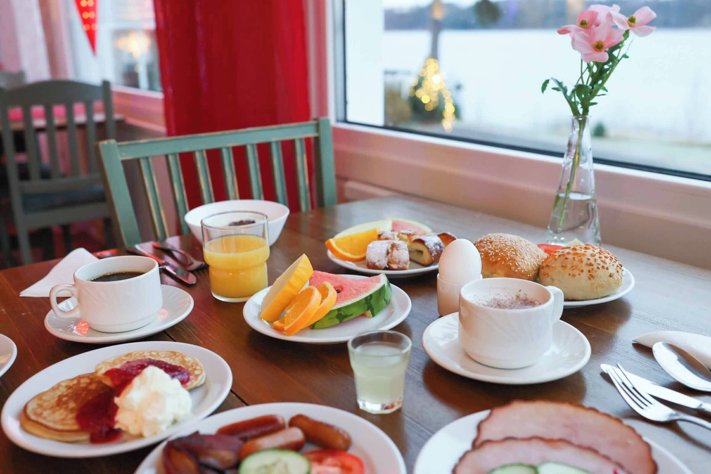 A breakfast table with various dishes, a cup of coffee, and a vase with flowers.