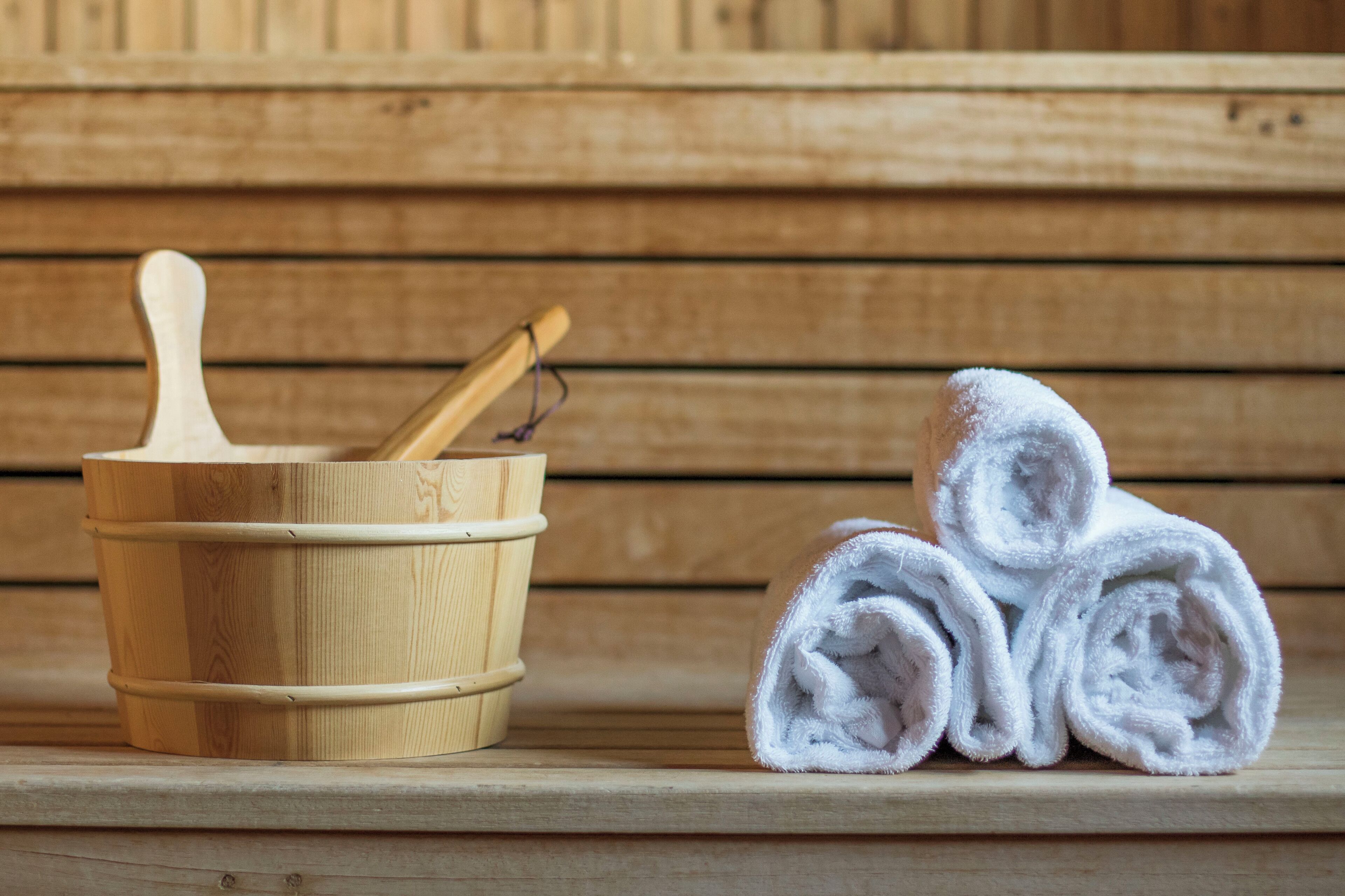 Une cuve en bois, une louche en bois et un seau en bois, ainsi que des serviettes blanches roulées posées sur un banc en bois.