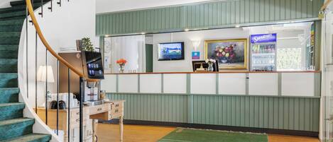 Un área de recepción con alfombra verde, una escalera con escalones color turquesa, una máquina de café y un televisor montado en la pared.