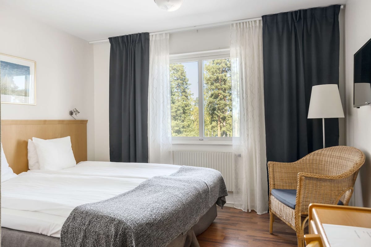 A hotel room with a large bed, a chair, a desk, and a window with curtains.