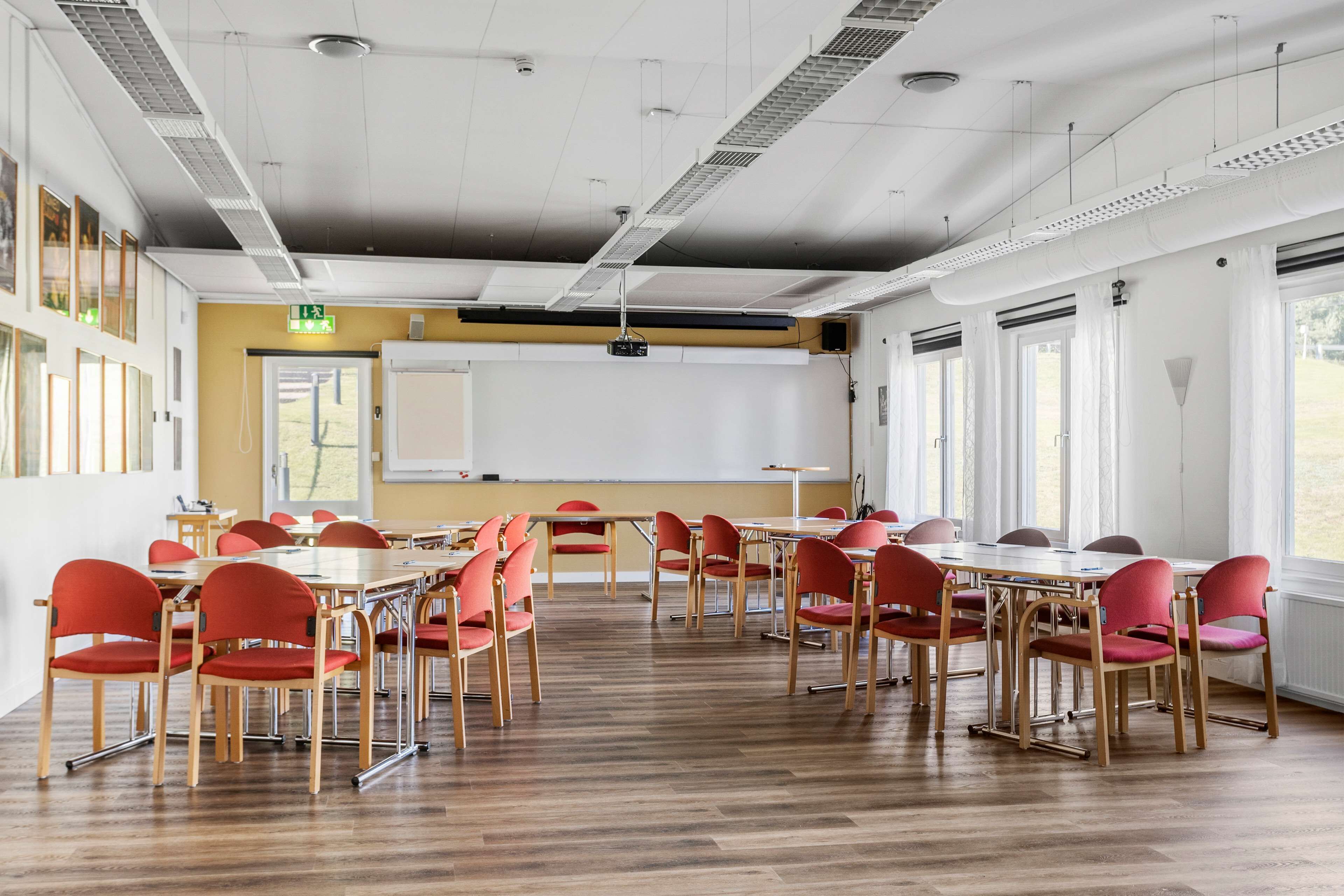 A conference room with wooden tables and red chairs, a whiteboard, and large windows.