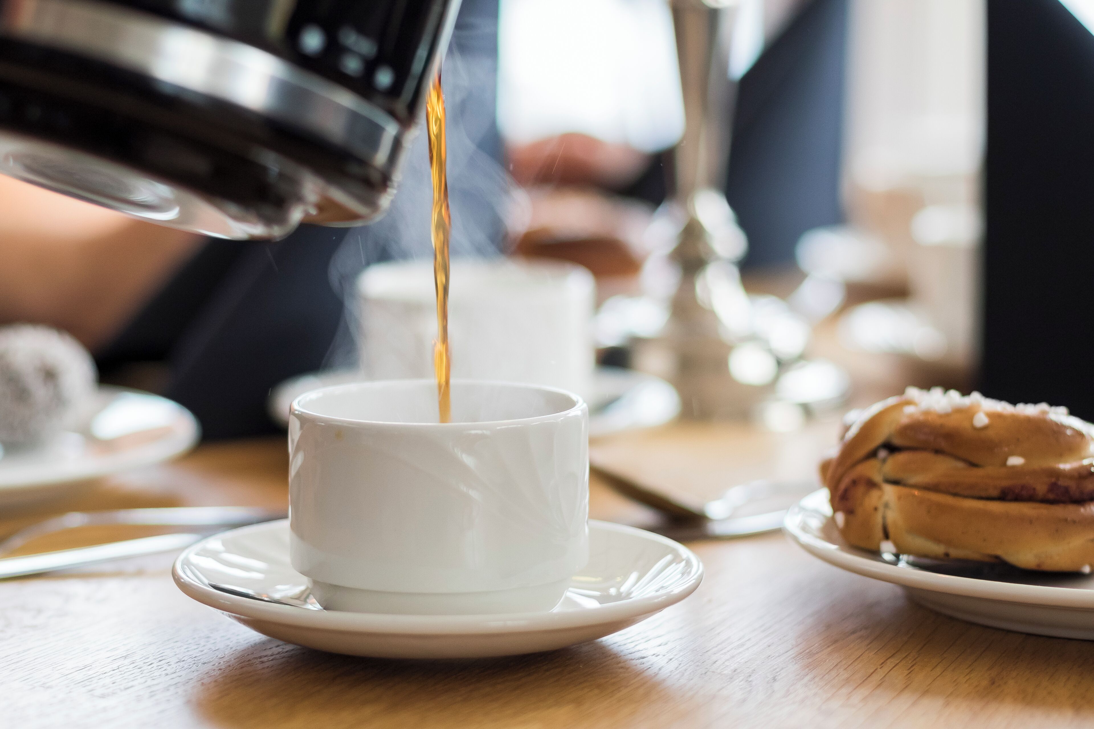 En kopp kaffe hälls upp i en vit kopp som står på ett litet fat.
