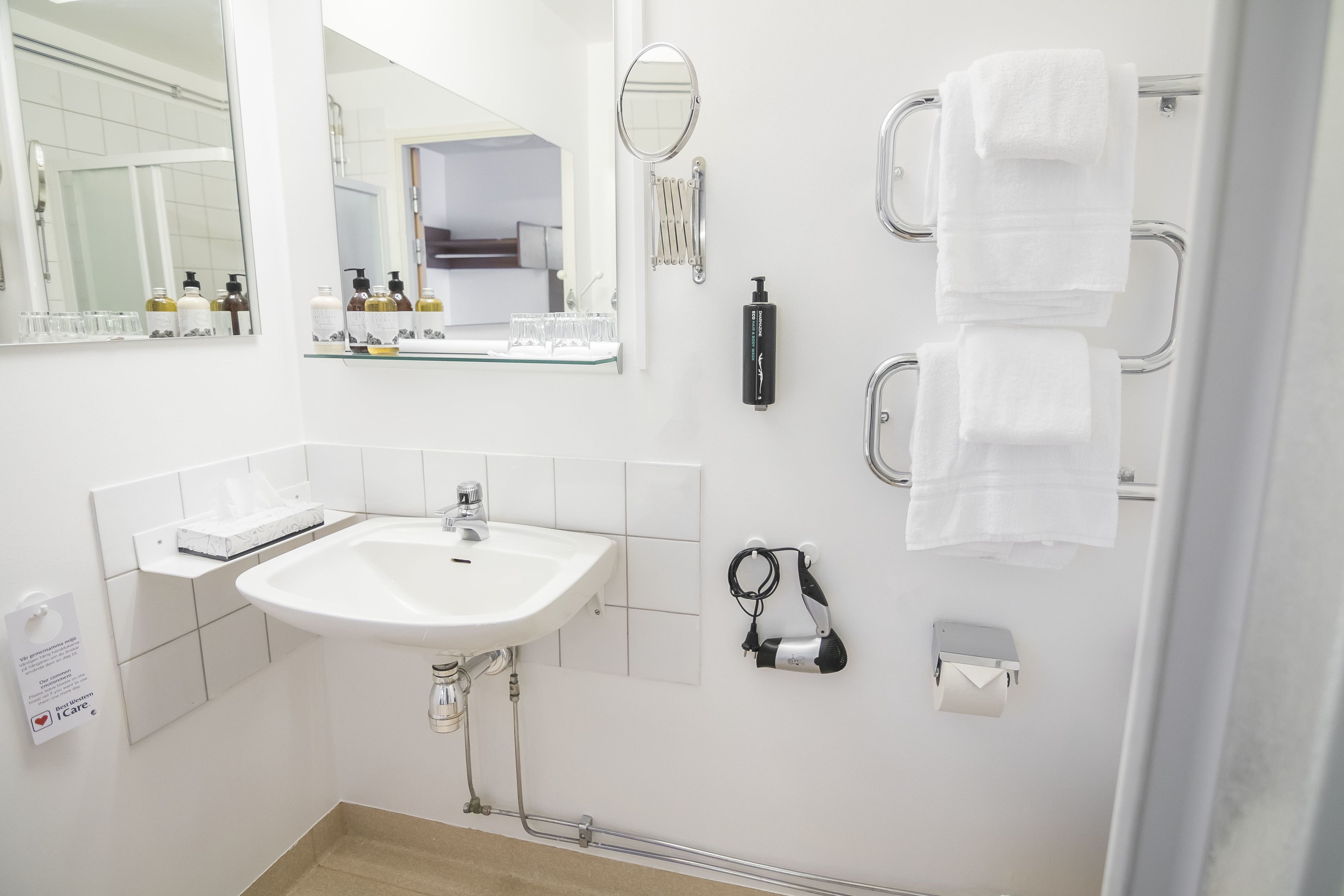 Une salle de bain moderne avec un lavabo blanc, un grand miroir, un porte-serviettes et une douchette à main.