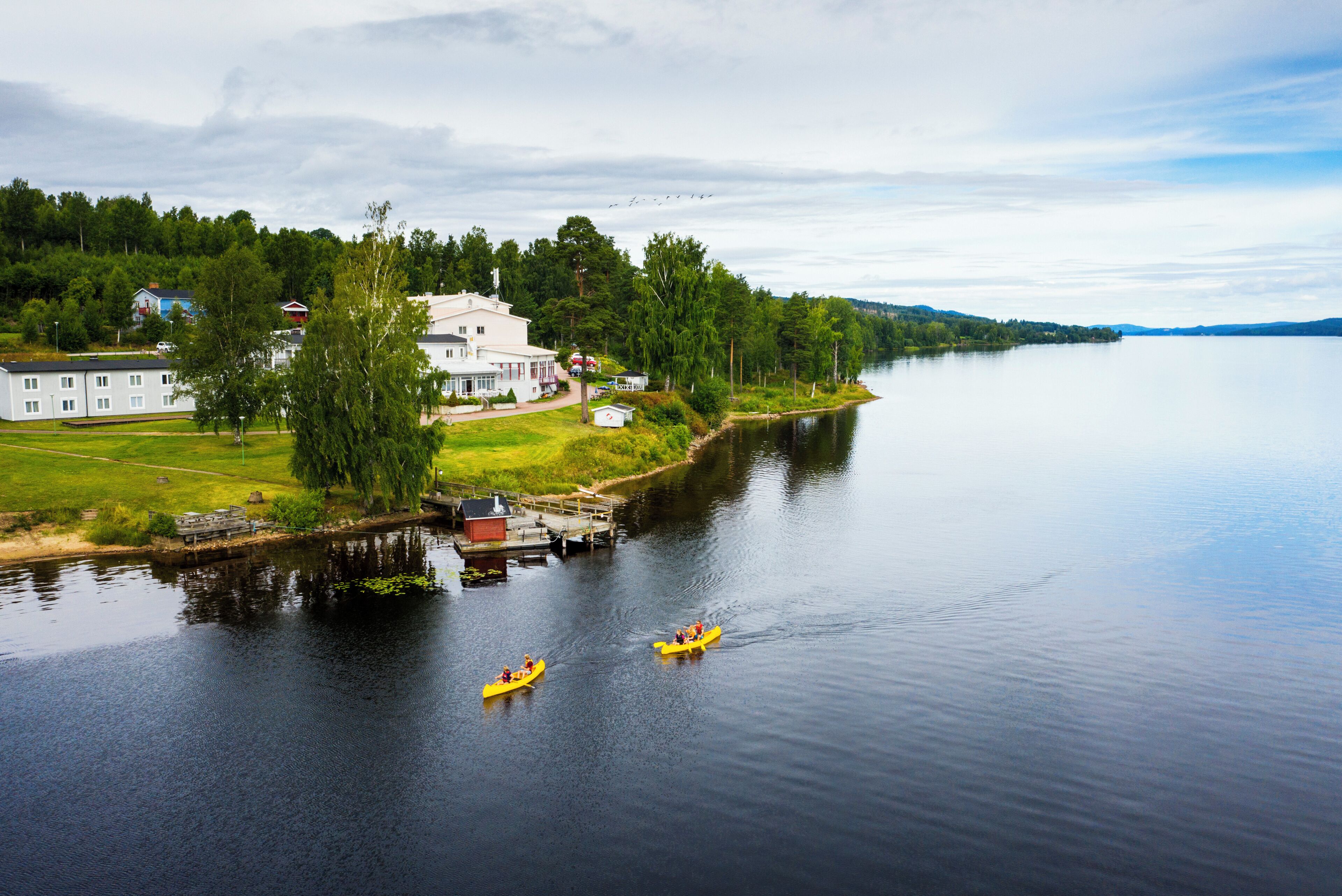 A calm lake with a dock and a large house on the shore.