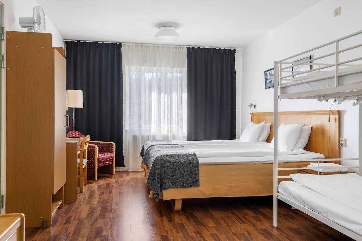 A hotel room with a bunk bed, a desk with a chair, a lamp, and a wardrobe.