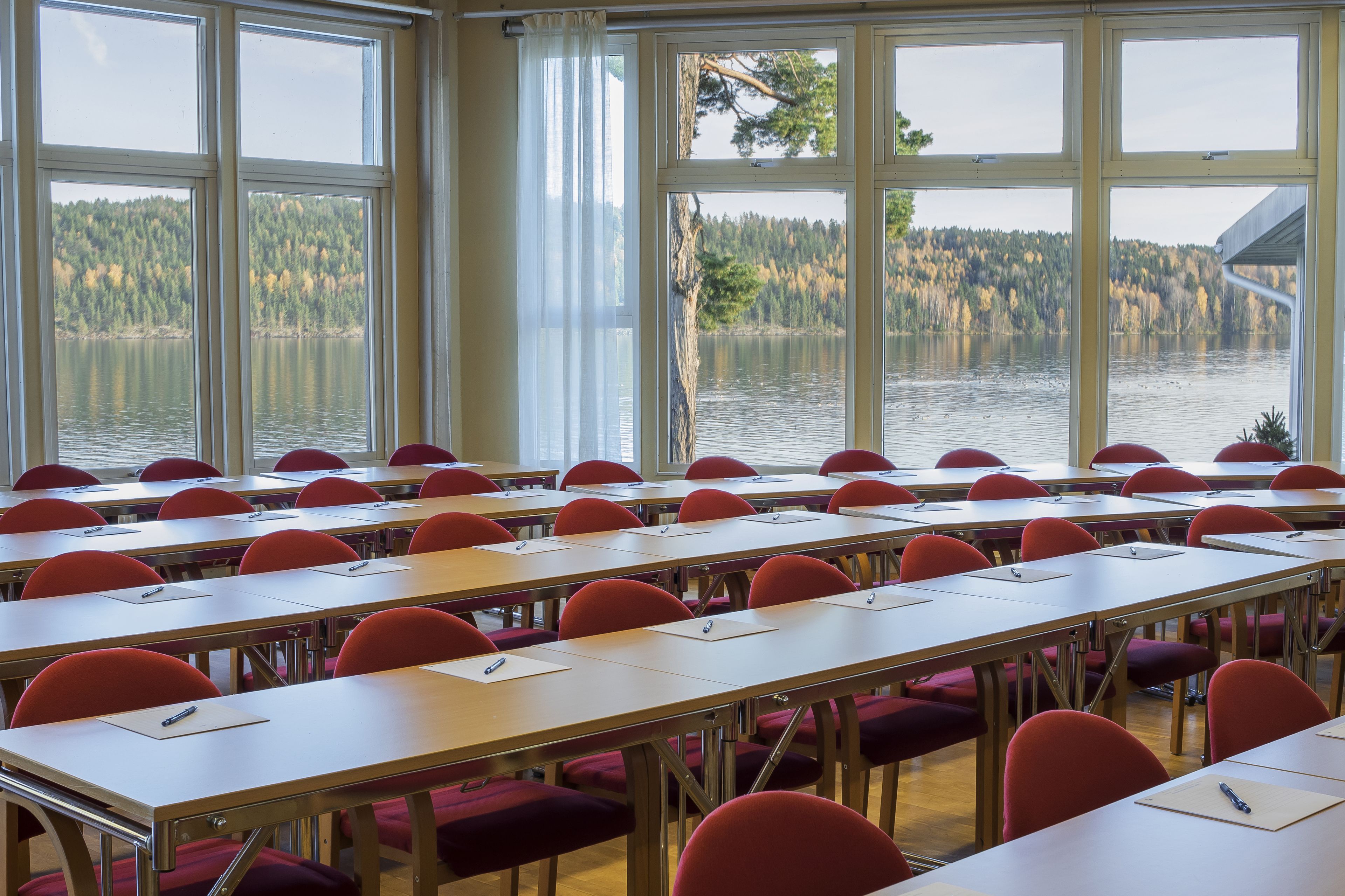 A classroom with rows of desks and chairs, large windows with a view of a lake and forest.