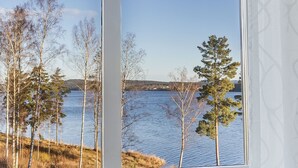 Ein Zimmer mit großem Fenster und Blick auf einen See und Bäume.
