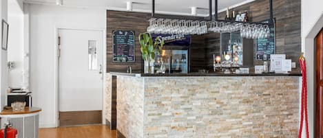 A modern bar area with a stone-textured counter, hanging wine glasses, and a menu board.